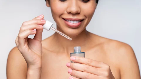 Close-up of a smiling woman applying niacinamide serum to her skin, showcasing the beauty and efficacy of this vital skincare ingredient.