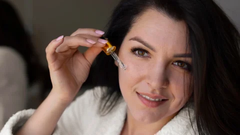 Close-up of a woman applying retinol serum to her face, highlighting the rejuvenating effects of retinol and retinoids in skincare.